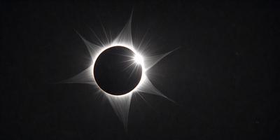 The primary subject of the image is a solar eclipse, with a large, dark sun surrounded by a bright, white corona. The setting is a dark sky, and the visual style is a photo. The colors and mood of the image are dramatic and intense, with the dark sun and bright corona creating a striking contrast against the night sky.