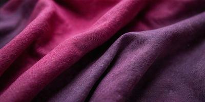 The primary subject of the image is a piece of purple fabric. The setting is a room with a pink background. The visual style is a close-up of the fabric, showcasing its texture and color. The dominant colors are purple and pink, creating a warm and inviting atmosphere.