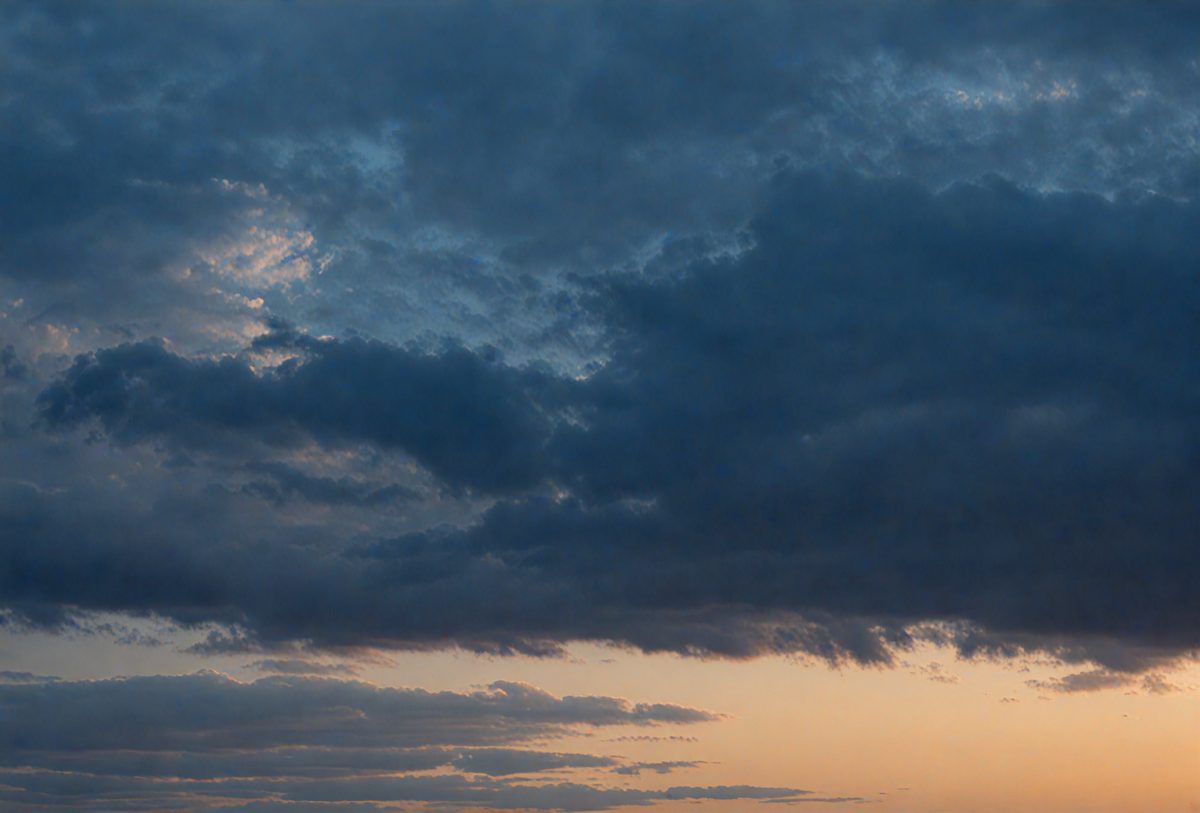 The primary subject of the image is a cloudy sky with dark clouds. The setting is a sunset, creating a dramatic backdrop. The visual style is a photo, capturing the beauty of the cloudy sky during the sunset. The colors and mood of the image are dominated by the dark clouds and the warm hues of the sunset, creating a moody and dramatic atmosphere.