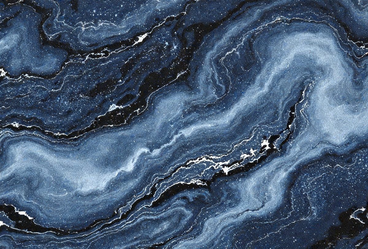 The primary subject of the image is a blue and black marbled stone. The setting is a dark blue background, which contrasts with the marbled stone. The visual style is a close-up of the marbled stone, showcasing its intricate patterns and textures. The colors and mood of the image are predominantly dark and moody, with the blue marbled stone serving as the focal point.