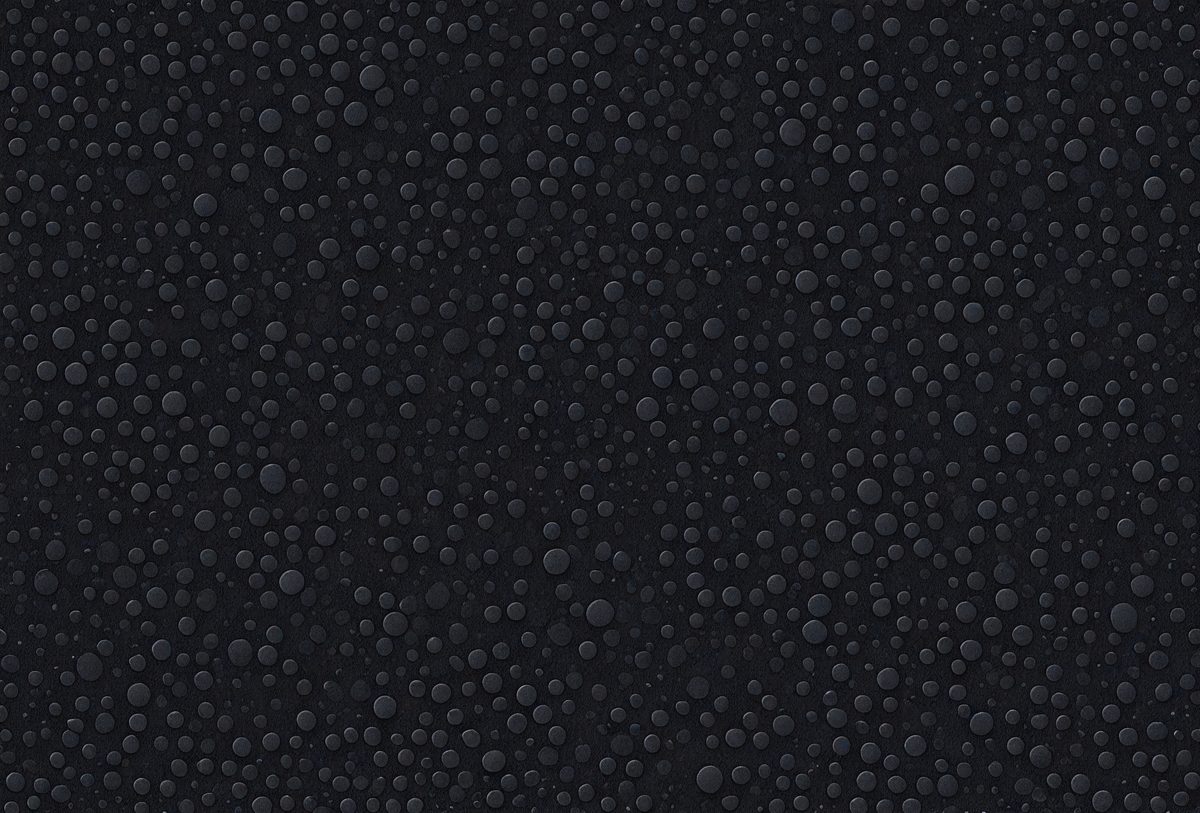 The primary subject of the image is a close-up of a black surface with a pattern of small bubbles. The setting is a dark room, and the visual style appears to be a photo. The dominant colors are black and white, and the overall atmosphere is somewhat mysterious and intriguing.