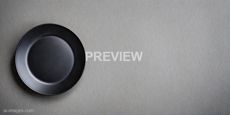 The image features a single black ceramic plate placed on a light beige textured surface. The plate is positioned towards the left side of the frame, with a significant amount of empty space on the right, emphasizing the minimalistic composition. The lighting creates subtle reflections and shadows, highlighting the smooth, curved edges of the plate against the textured background.